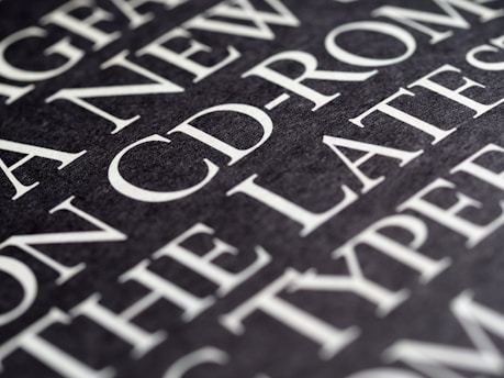 A close-up view of text on a dark background, featuring large, bold, white typography. The text appears to be printed on a textured surface, with words such as 'CD-ROM' clearly visible.