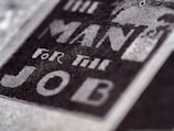 Close-up of text reading 'The Man For The Job' in bold, prominent letters on a textured surface, suggesting a vintage or classic style.