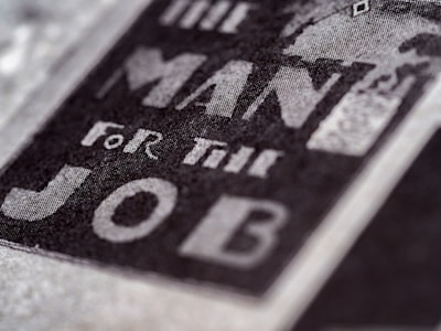 Close-up of text reading 'The Man For The Job' in bold, prominent letters on a textured surface, suggesting a vintage or classic style.
