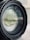 A close-up view of a camera lens, showing the concentric circles and reflections on the glass surface. The lens casing appears black and sturdy, with fine details of the aperture and elements visible through the glass.