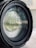 A close-up view of a camera lens, showing the concentric circles and reflections on the glass surface. The lens casing appears black and sturdy, with fine details of the aperture and elements visible through the glass.