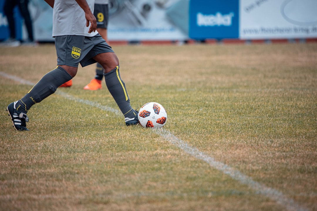 man in blue and white soccer jersey kicking soccer ball on green grass field during daytime