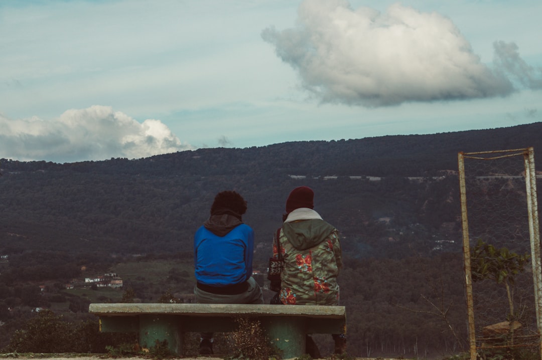 2 person sitting on concrete bench looking at the mountains during daytime