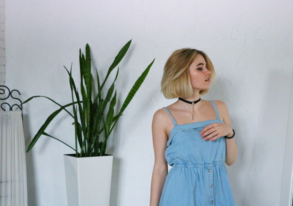 woman in blue spaghetti strap dress standing beside green plant