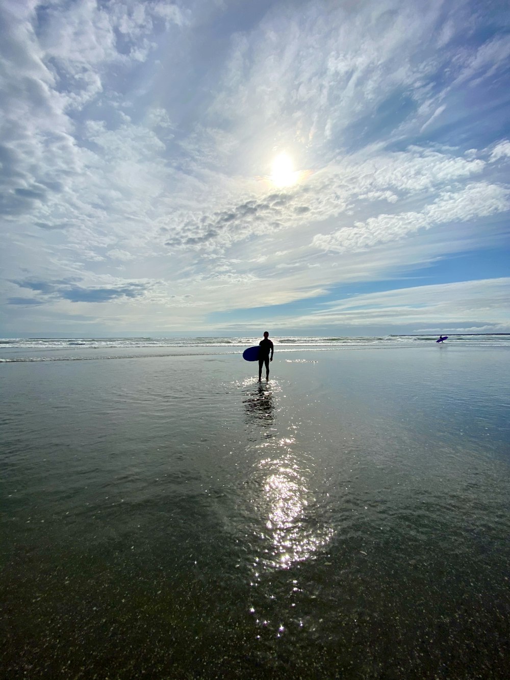 person in black jacket walking on sea shore under blue and white sunny cloudy sky during