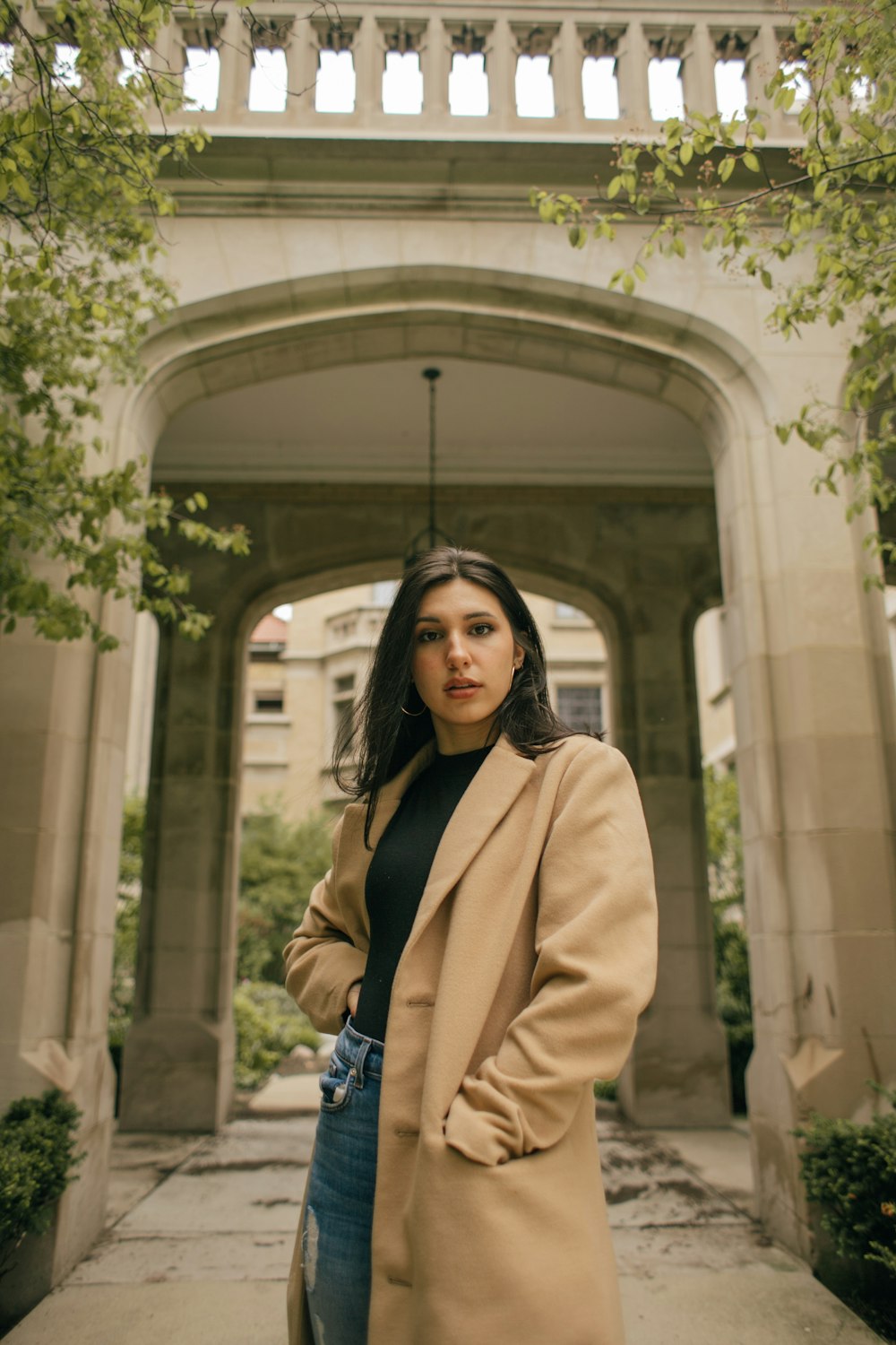 woman in brown coat standing near white concrete building during daytime