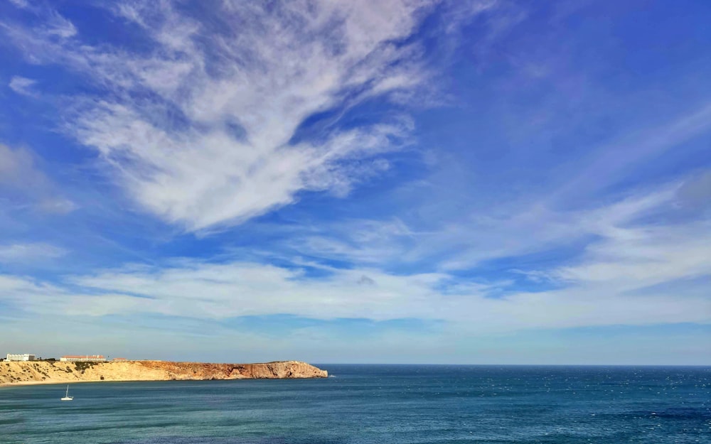 brown rock formation on sea under blue sky and white clouds during daytime