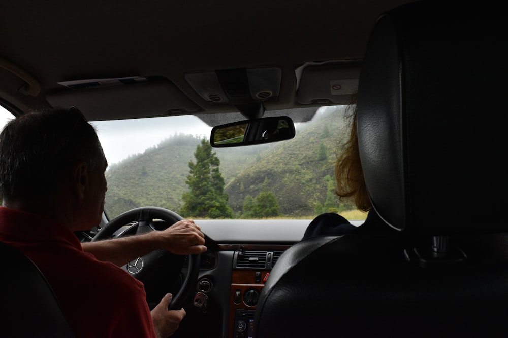 man in red shirt driving car during daytime