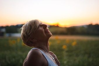 woman in white tank top looking at the sunset