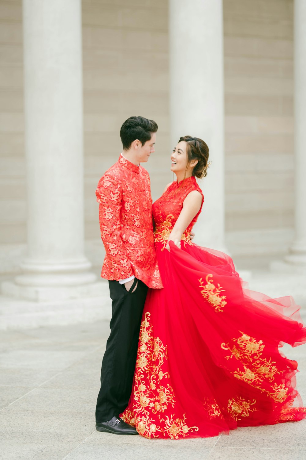 a man and a woman in red and gold dress standing next to each other