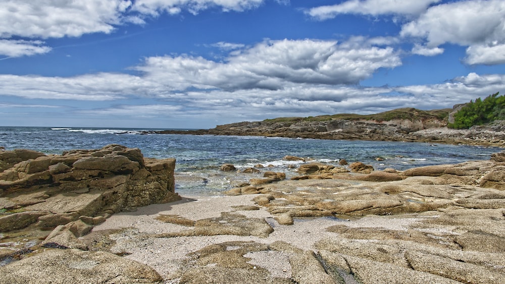 brown rocks on seashore under blue sky and white clouds during daytime