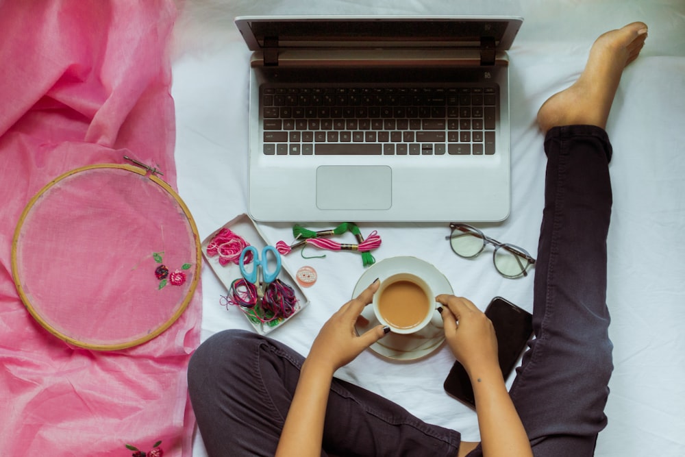 person holding white ceramic mug near macbook pro