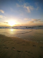 Sunset view over a peaceful beach with footprints in the sand.