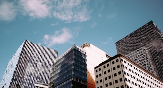 A cluster of modern skyscrapers with glass and steel structures, reaching towards a partly cloudy blue sky.