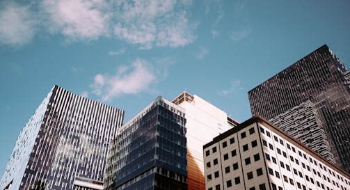 A cluster of modern skyscrapers with glass and steel structures, reaching towards a partly cloudy blue sky.
