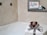 A luxurious bathroom setup features a stack of white towels elegantly tied with a patterned ribbon, topped with a decorative item. In the background, a soft glow from a lit candle and a framed sign reading 'Natural Soaps' enhance the ambiance. The setting conveys a sense of relaxation and indulgence.
