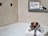 A luxurious bathroom setup features a stack of white towels elegantly tied with a patterned ribbon, topped with a decorative item. In the background, a soft glow from a lit candle and a framed sign reading 'Natural Soaps' enhance the ambiance. The setting conveys a sense of relaxation and indulgence.
