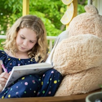 girl in blue and white long sleeve shirt sitting on brown bear plush toy