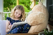 girl in blue and white long sleeve shirt sitting on brown bear plush toy