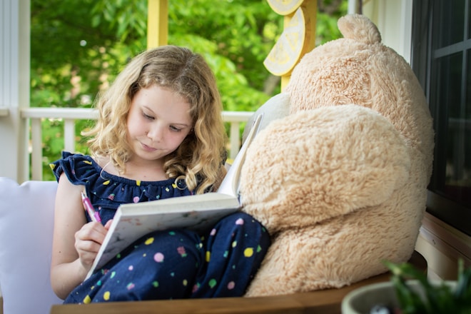 girl in blue and white long sleeve shirt sitting on brown bear plush toy