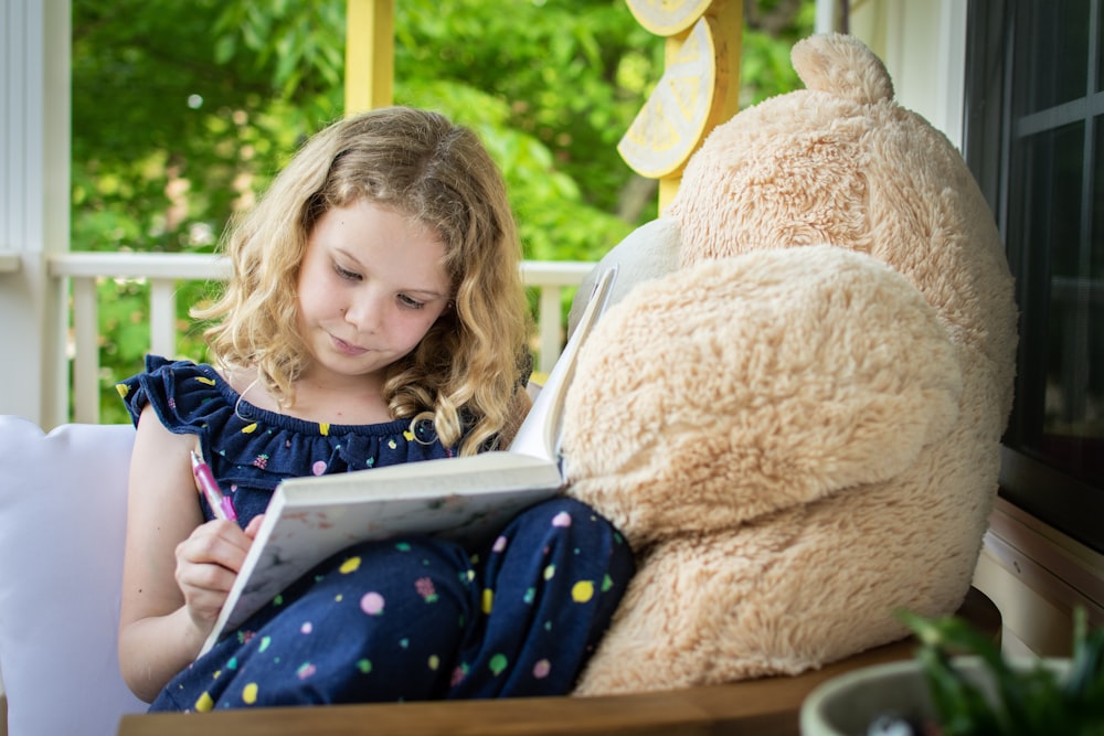 fille en chemise à manches longues bleue et blanche assise sur un ours brun jouet en peluche