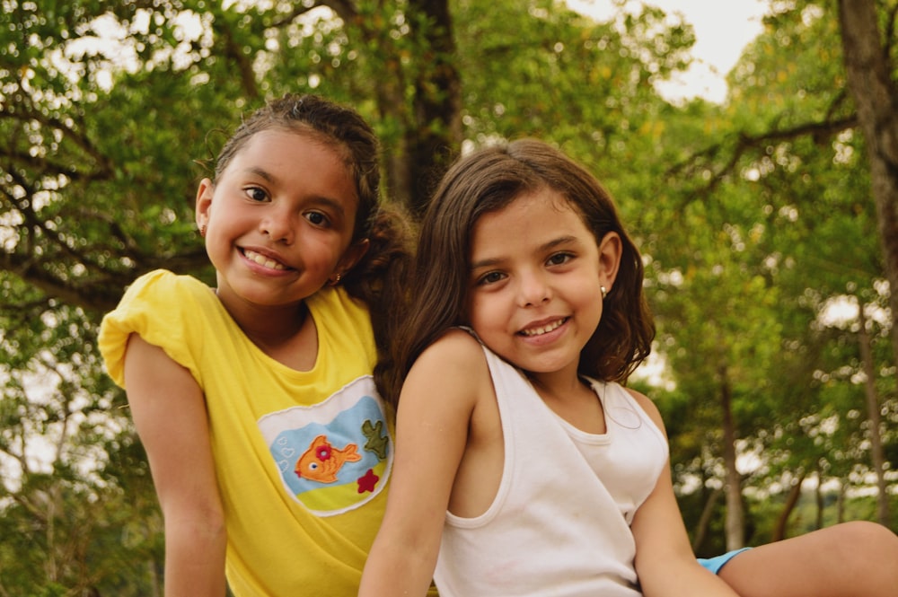 2 girls smiling and standing near green trees during daytime