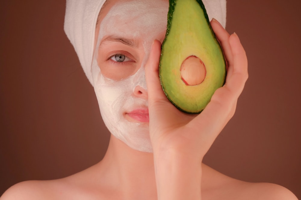 緑の果物を持つ白いフェイスマスクを持つ女性