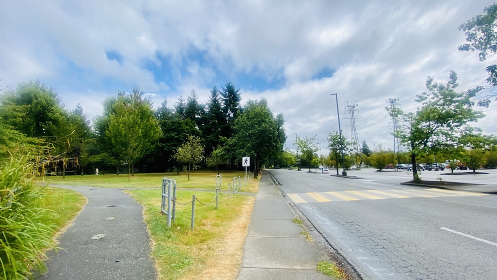 gray concrete road between green trees under blue sky and white clouds during daytime