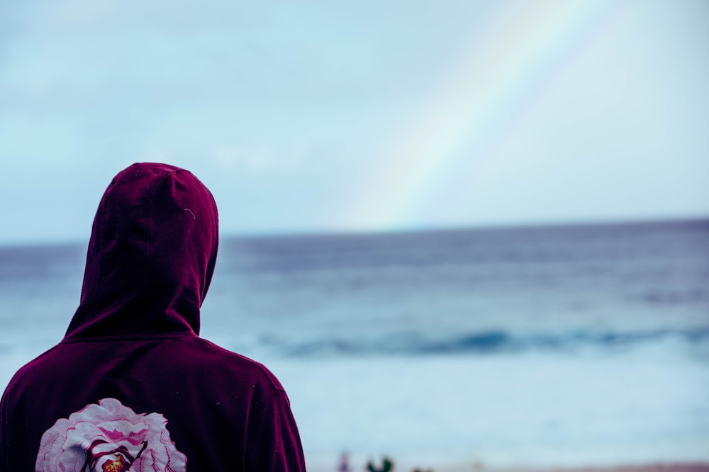person in red hoodie standing near sea during daytime
