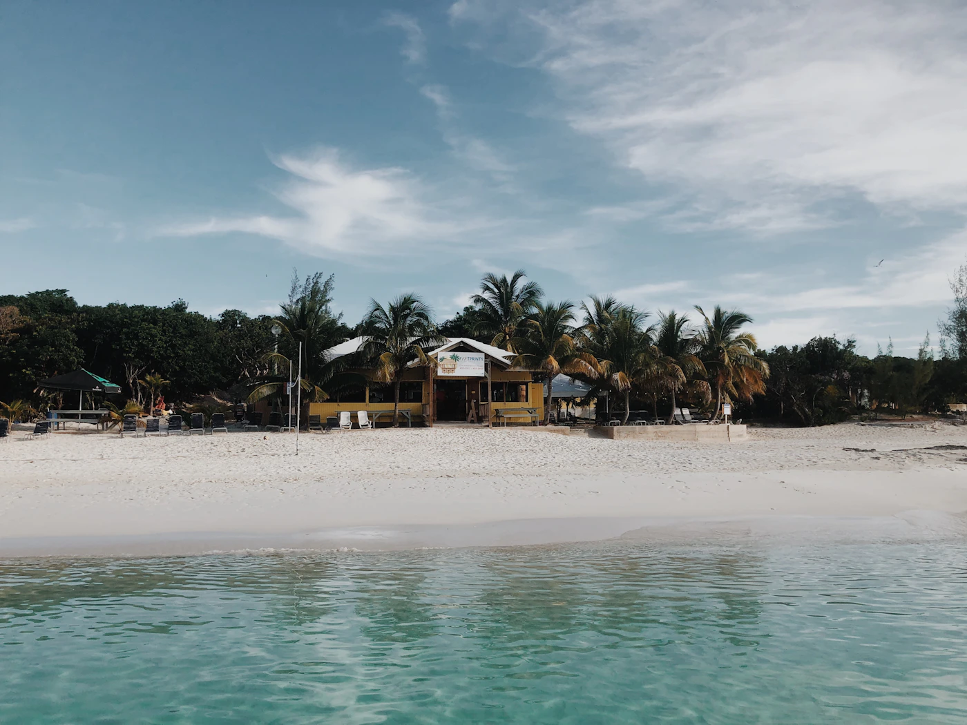 A beautiful white sand beach in the Bahamas with clear shallow water and the deeper turquoise and blue of the Bahamian banks visible beyond under a partly cloudy Caribbean sky