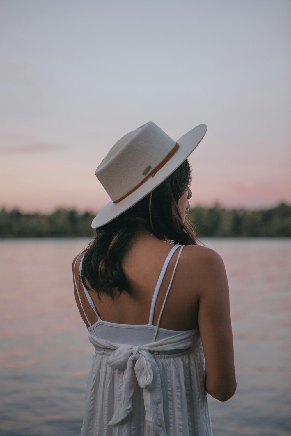 woman in white spaghetti strap top wearing white sun hat standing near body of water during