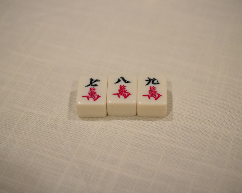 Three Mahjong tiles are placed in a row on a textured, off-white surface. The tiles each display Chinese characters in black and red ink.