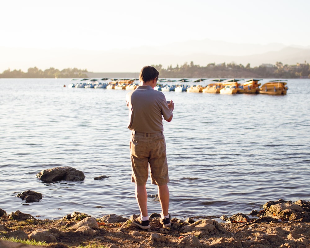 man in gray shirt and brown shorts standing on rocky shore during daytime