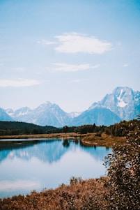 lake surrounded by trees and mountains under blue sky during daytime