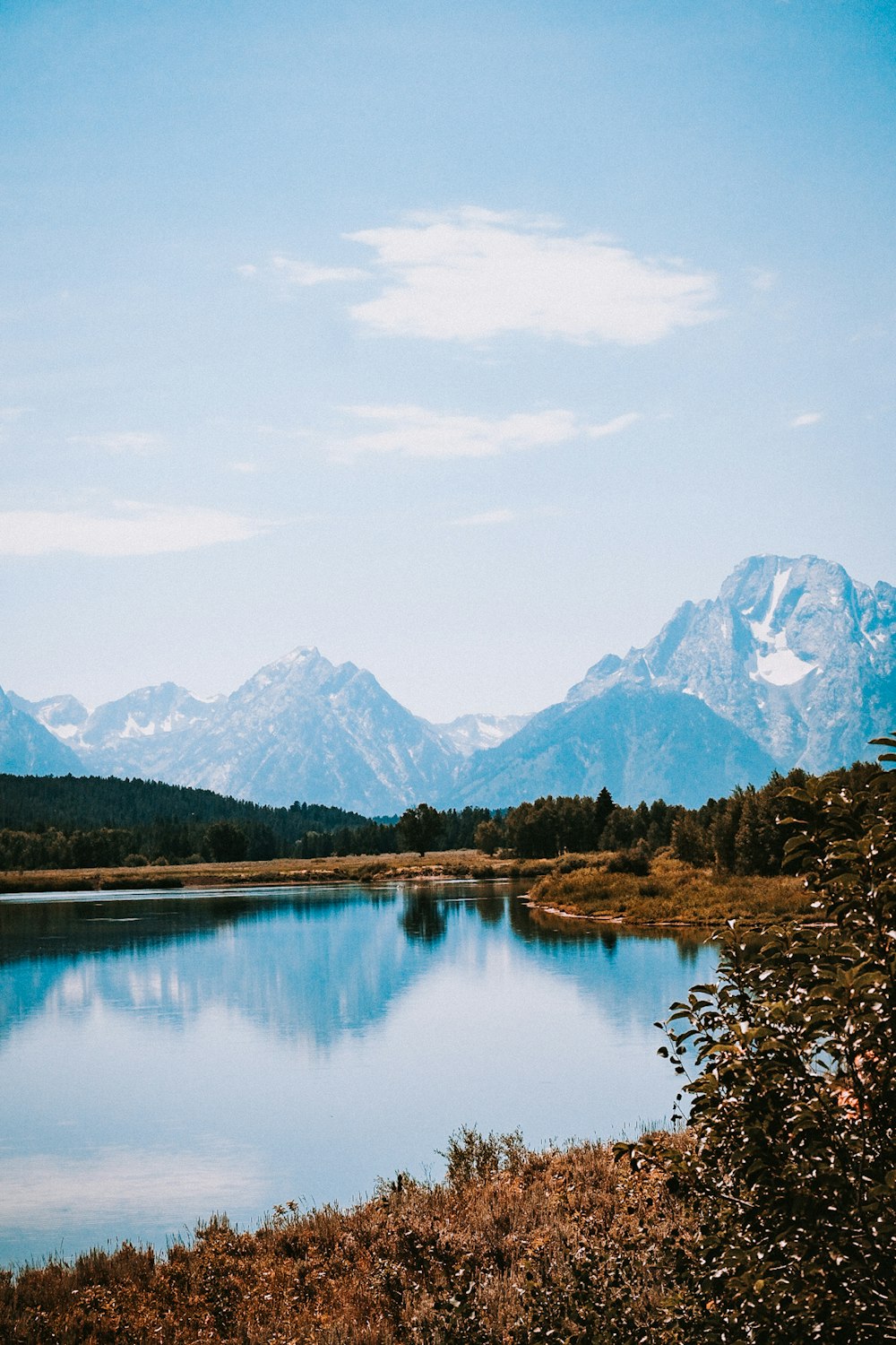 lake surrounded by trees and mountains under blue sky during daytime