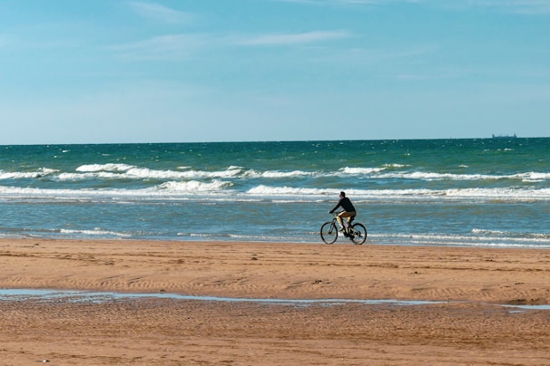 A biker riding along a sandy beach with waves crashing in the background.