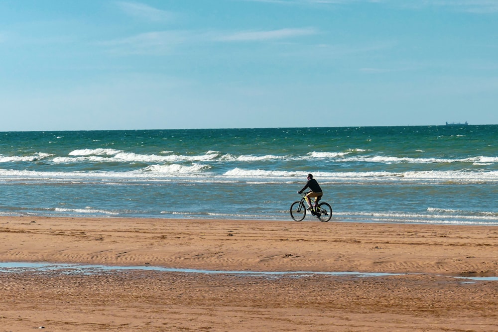 man in black shirt riding bicycle on beach during daytime