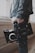 A person holds a professional video camera, wearing a denim jacket. The camera appears to be a high-end model, possibly used for filmmaking or professional video production.