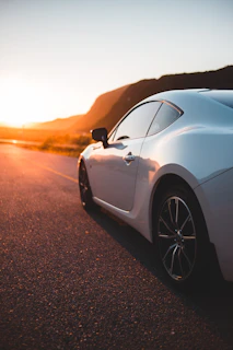A sleek sports car parked on a winding mountain road at sunset, with warm light highlighting its curves.