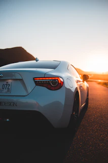 Dynamic photo of an automotive influencer filming a high-end car on a winding mountain road at sunset.