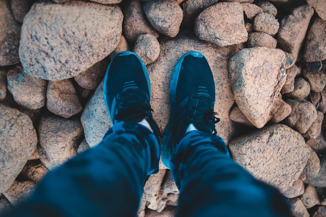 person in blue pants and blue sneakers standing on rocky ground