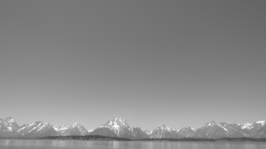 A panoramic view of the snow-capped Swiss Alps with a crystal-clear lake reflecting the mountains under a bright blue sky.