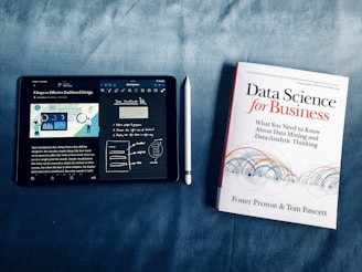 An iPad displaying data visualization content next to a book titled 'Data Science for Business.' The iPad is showing notes and a diagram about dashboard design, accompanied by a stylus placed between the iPad and the book.