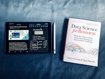 An iPad displaying data visualization content next to a book titled 'Data Science for Business.' The iPad is showing notes and a diagram about dashboard design, accompanied by a stylus placed between the iPad and the book.