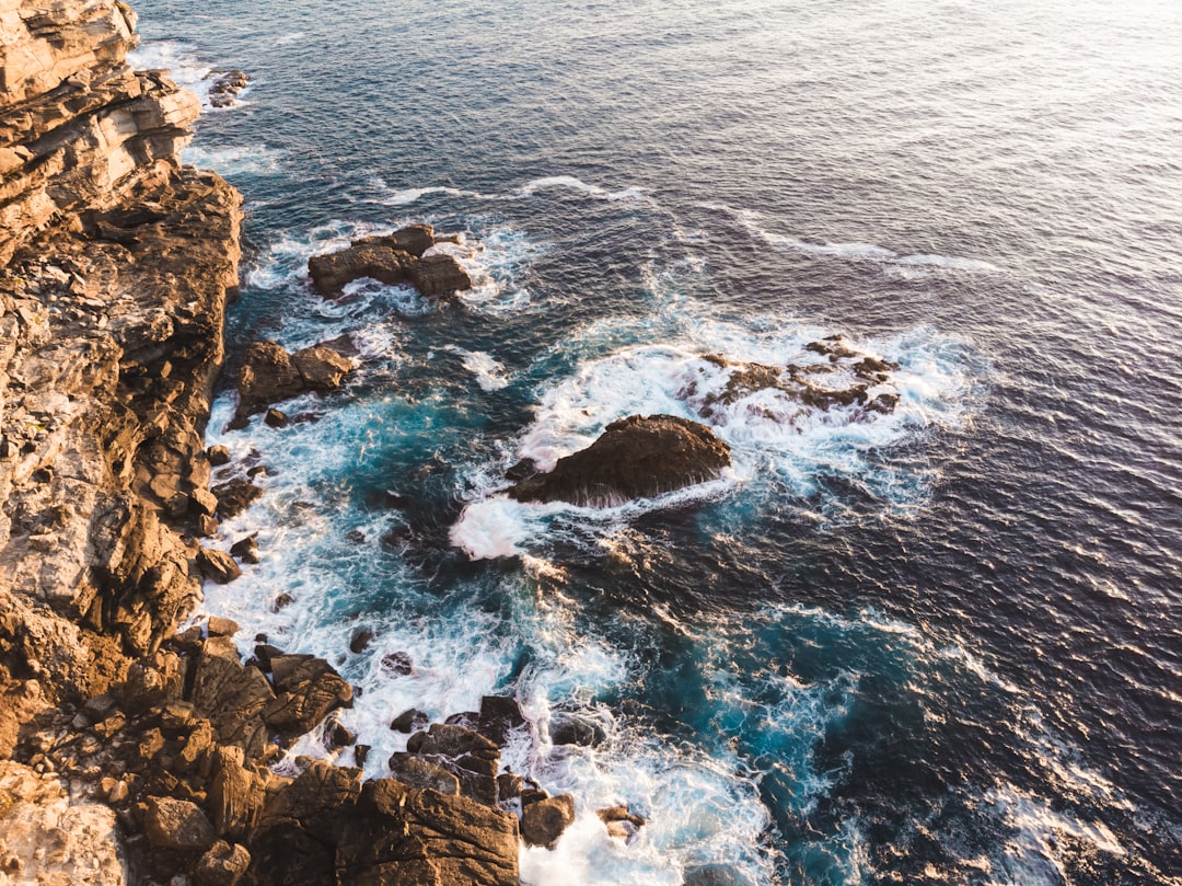 brown rocky mountain beside blue sea during daytime