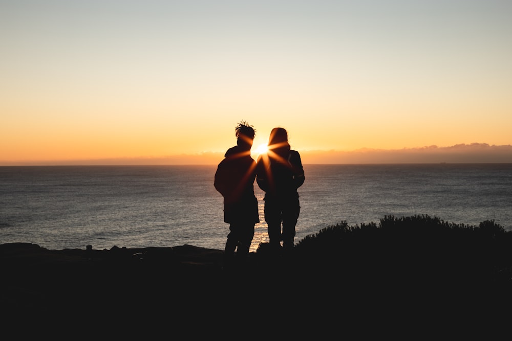 silhueta do homem e da mulher em pé na colina durante o pôr do sol