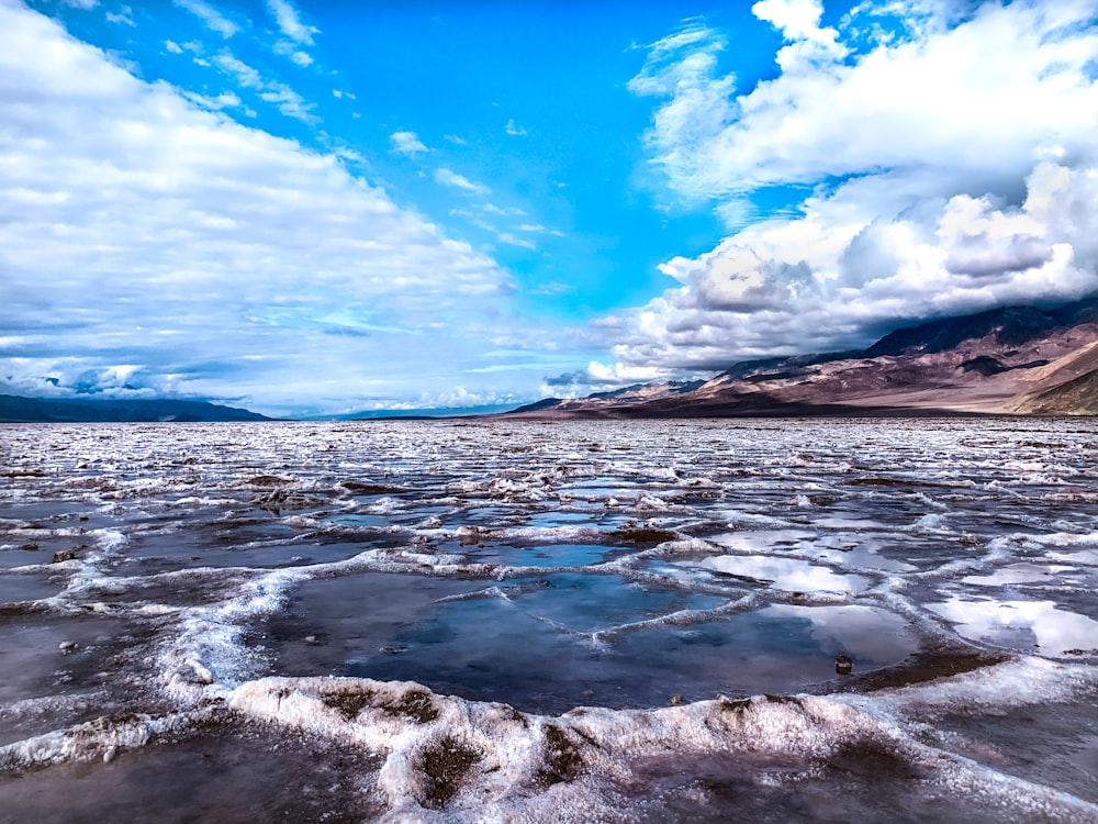 ocean waves crashing on shore under blue and white cloudy sky during daytime