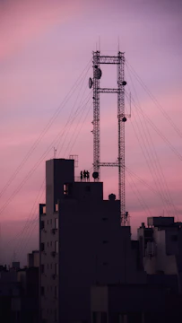 Engineers installing 5G antennas on a city rooftop at sunset.