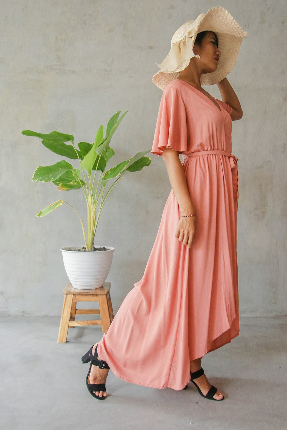 woman in orange dress wearing brown sun hat standing near green potted plant