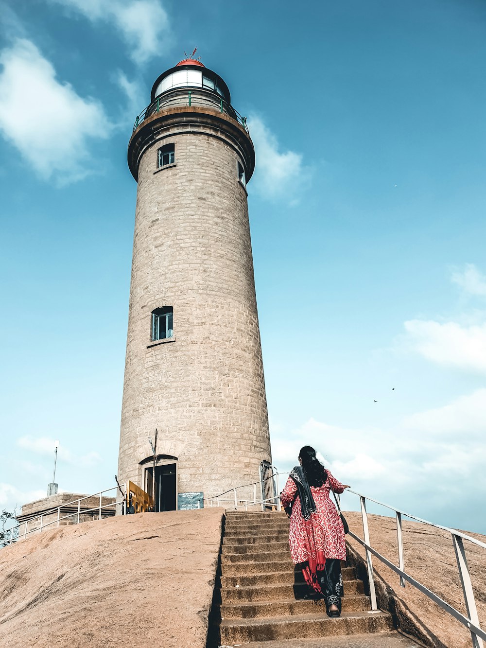 people walking on brown wooden dock near brown concrete lighthouse under blue sky during daytime